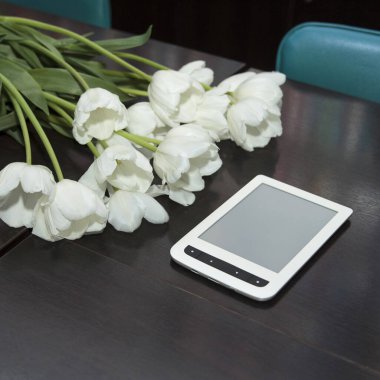 Seyirciler arasında bir buket beyaz lale ve siyah ahşap bir masada beyaz bir elektronik okuyucu.