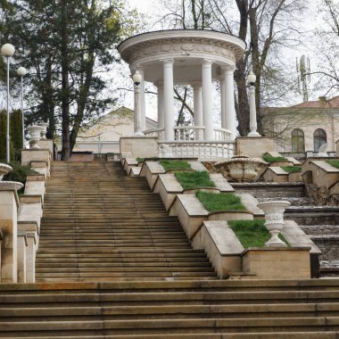 Süslü balyaları ve bitkileri olan büyük taş basamaklar manzaralı bir şehir parkında klasik beyaz bir kubbeye çıkıyor.