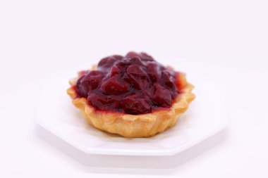 Lezzetli tatlı, kremalı ve şuruplu kiraz sepeti tatlı tabağında beyaz bir arka planda duruyor.