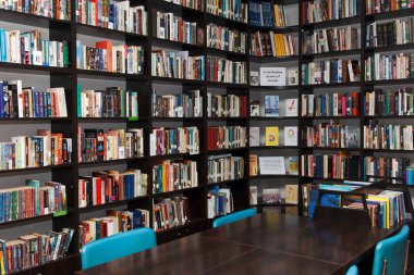 CHISINAU, MOLDOVA - 14 Mart 2025; Uzun ahşap masalar, mavi sandalyeler ve seramik zemin üzerinde eğitim ve bilgiyi sembolize eden kitaplarla dolu rahat kütüphane içi