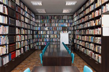 CHISINAU, MOLDOVA - 14 Mart 2025; Uzun ahşap masalar, mavi sandalyeler ve seramik zemindeki kitaplarla dolu kütüphane iç mimarisi, eğitimi ve bilgiyi simgeliyor