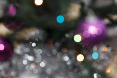 Renkli süsleri ve yanıp sönen ışıkları olan bir Noel ağacının bulanık arkaplanı. Sahne şenlikli bir tatil atmosferi sunuyor..