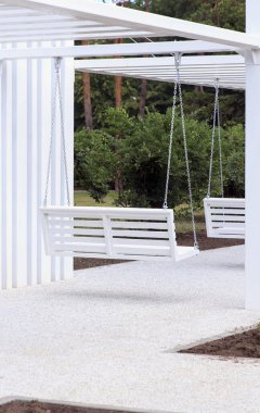 Minimalist bir yapının altında beyaz salıncakların olduğu modern bir açık hava alanı. Bölge yeşilliklerle çevrili, sakin bir ortam yaratıyor.