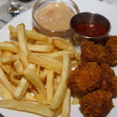 Altın patates kızartması ve beyaz tabakta çıtır tavuk nugget ketçap ve kremalı sos, ahşap bir masada fotoğraflanmış.