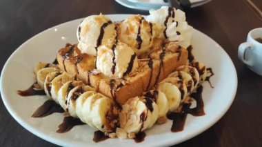 Ballı tost, vanilyalı dondurma ve çikolata sosuyla servis edilen muz dilimleri ve beyaz mermer masada çırpılmış krema..