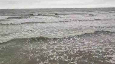 Huzurlu dalgalar Idyllic doğal arka planda akıyor. Koyu deniz ve beyaz köpük. Okyanus dalgalarının şafak vakti kıyıya çarptığını gösteren görüntüler. Hüzünlü bir gün