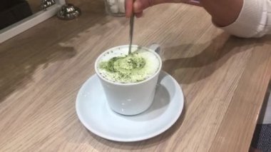 Asyalı bir kadın Japon çayını mavi bir fincanla kaşıkla karıştırıyor. Tahta masada sağlıklı yeşil çay, sıcak yeşil çay.