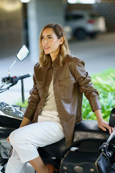 Dorosła Motocyklistka Stylowych Ubraniach Odwracając Wzrok Siedząc Motocyklu Rozmytym Tle — Zdjęcie stockowe