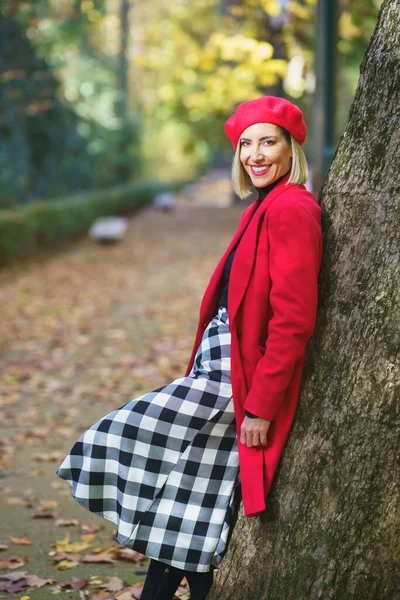 秋天公园的人行道上 身穿雅致服装 靠在树上 看着相机的微笑女性的侧影 — 图库照片