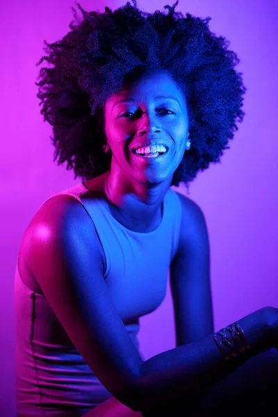 Szczęśliwa Afroamerykanka Kręconymi Włosami Uśmiechnięta Patrząca Kamerę Pod Fioletowym Neonem — Zdjęcie stockowe