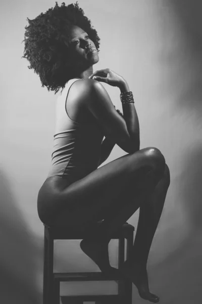 身穿紧身衣的非洲裔美国女模特的侧视图 卷曲的头发接触肩膀 坐在凳子上看着别处 黑白照片 — 图库照片