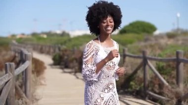 Cuban woman with afro hair, dancing on a wooden path near the beach. Positive female with joy doing Cuban salsa moves.