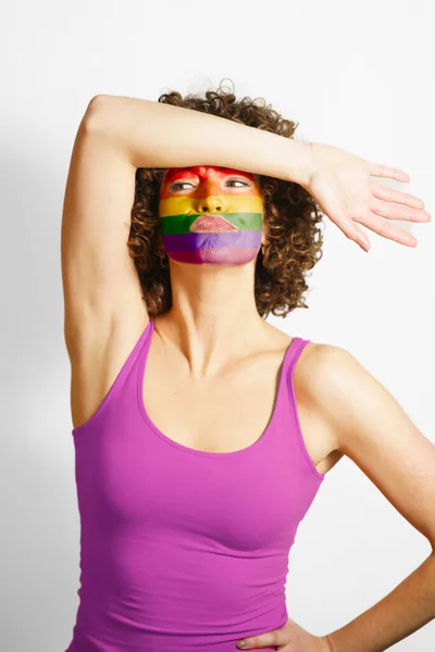 年轻的卷发女子 手放在额头上 脸上涂着彩虹色 站在演播室的团结和宽容的概念下 望着远方 — 图库照片