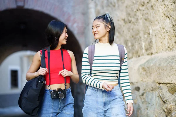 バッグやフォトカメラを見ながら 荒々しい壁の近くを歩いていると カジュアルな服装で幸せな若いアジアの女性観光客 — ストック写真