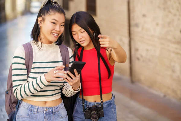 20代のアジアの女の子たちは 携帯電話で地図を使用してグラナダ市内を旅し 一緒に旅行中に方向を探しながら指摘 — ストック写真