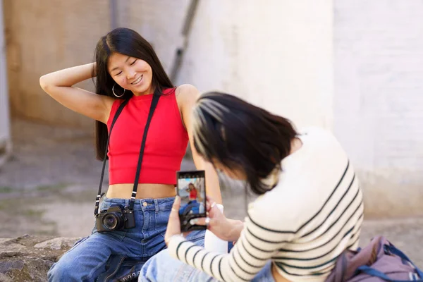 観光中にストライプセーターで彼女の前で写真をポーズしながら 赤い上に正の若い民族の女性とジーンズは髪に触れます — ストック写真
