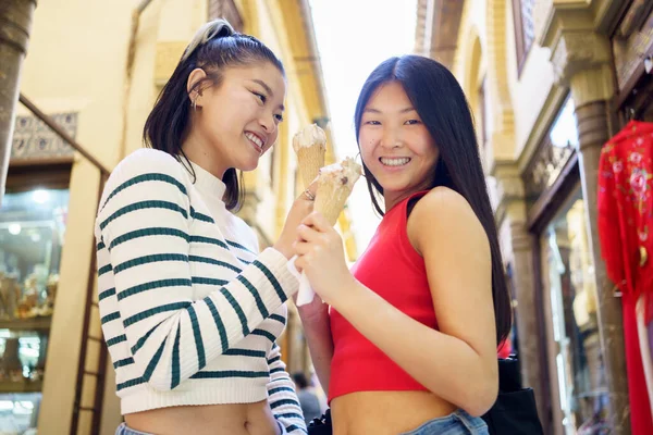 路上で立ちながらおいしいアイスクリームを食べ 昼間は一緒に時間を楽しむアジアの女性の友人の低角度 — ストック写真