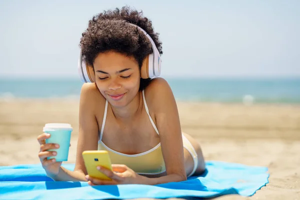 Afro Saçlı Şık Bikini Kulaklıklı Akıllı Telefondan Kahve Içen Kumlu — Stok fotoğraf