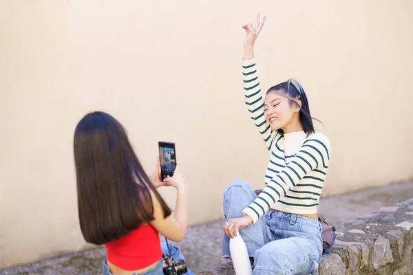 幸せな若いアジアの女性観光客が一緒に休暇中に街の石の境界線に座っている間にスマートフォンで写真を撮る — ストック写真