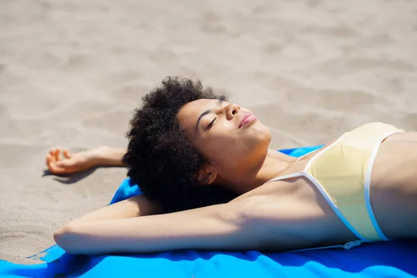 幸せな若いですアフリカ系アメリカ人女性観光客で巻き毛で流行ビキニで目を閉じて砂浜に横たわっている夏休み中に日光浴 — ストック写真