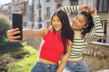 Granada 'daki şehir binalarına karşı cep telefonuyla selfie çekerken mutlu bir şekilde gülümseyen genç etnik Asyalı kız arkadaşlar.