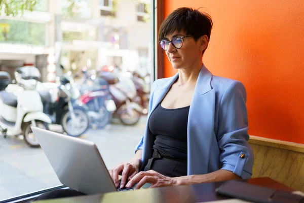Skoncentrowany Kobiecy Przedsiębiorca Formalnych Ubraniach Okularach Siedzący Przy Stole Laptopem — Zdjęcie stockowe