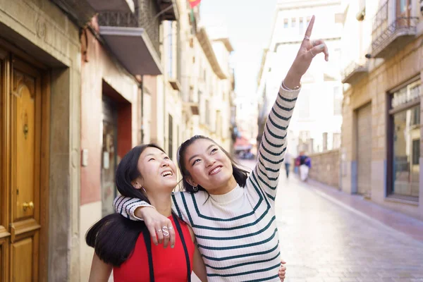 幸せなアジアのガールフレンドカジュアルな服の古い町の通りを歩くと晴れた日に指して抱擁しながら建物を見る — ストック写真