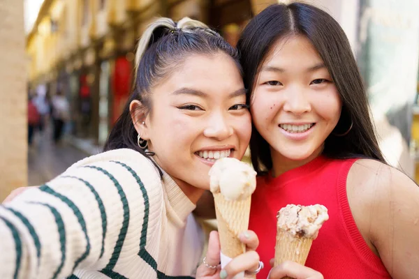 スペインのグラナダの典型的な通りでアイスクリームコーンを食べながら 2人の若い中国の女の子が自撮りをしています ヨーロッパを旅するアジア人の概念 — ストック写真