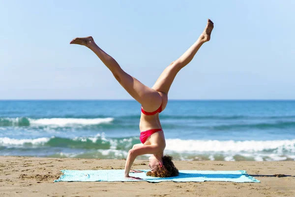 海の海岸で一人でセッションを持っている間にビキニで穏やかな女性のサイドビューを実行Tripod Headstand — ストック写真