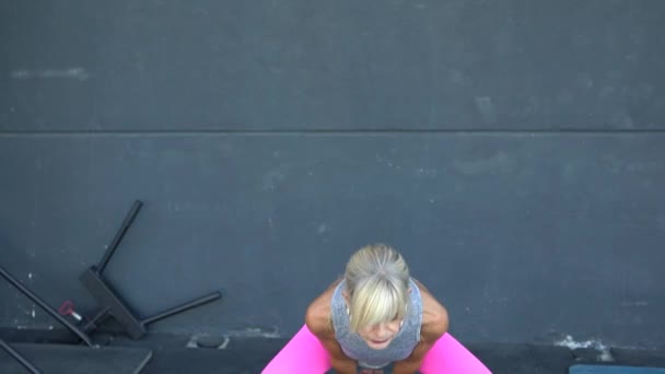 スポーツクラブでの重量挙げトレーニング中に灰色の壁に対して運動しながら重いケトルベルを持ち上げるアクティブウェアで魅力的な女性のリアルタイム — ストック動画