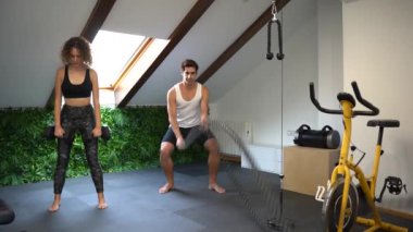 Yetişkin bir çiftten ağır çekimde spor salonunda ekipmanla çalışırken kadınlar öne eğilirken halatlarla ve gündüz dövüş halatlarıyla erkek antrenmanı yapıyorlar.