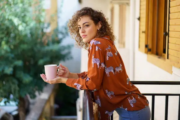 侧面看年轻女性穿着休闲服 靠着阳台栏杆朝外看 在模糊的背景下拿着咖啡杯 — 图库照片