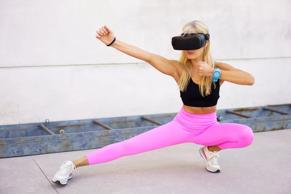 Full body of fit female in VR goggles performing kung fu fighting stance while practicing martial arts during virtual training outdoors