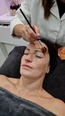 Güzellik salonundaki konteynırdan rahatlamış bir kadının yüzüne nemlendirici sürerek gerçek zamanlı bir güzellik uzmanı.