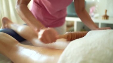 Klinikteki fizyoterapi seansı sırasında yatakta yatan tanınmayan bir kadın hastanın bacağında ahşap terapi mesajı veren kimliği belirsiz kadın masözün yavaş hareketi.