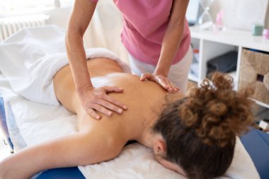 Yüksek ekin açılı pembe üniformalı kadın osteopat iyileşme sürecinde kanepede uzanan kadına masaj yapıyor.