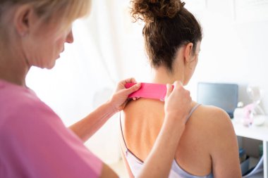 Ekin, klinikteki fizyoterapi seansı sırasında tanınmayan genç bir kadının ensesine kineziyoloji bandı uygulamaya odaklanmış.