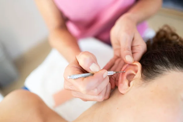 Crop professional chiropractor applying auriculotherapy ear acupuncture techniques of female client lying in modern clinic during health care routine