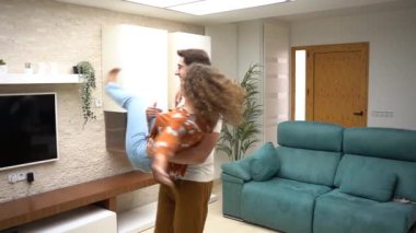 Erkeğin elinde dişiyi taşırken ve gün ışığında oturma odasında öpüşürken birbirlerine bakan neşeli yetişkin çiftin yavaş çekim tarafı.