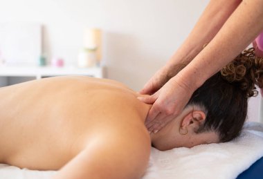 Anonim masaj terapistinin, modern spa salonundaki randevusu sırasında çıplak bir hastanın boynunu ovmasının yan görüntüsü.