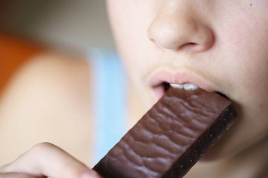Yukardan, evde besleyici protein barını ısıran isimsiz ergen kızın yakın planından.