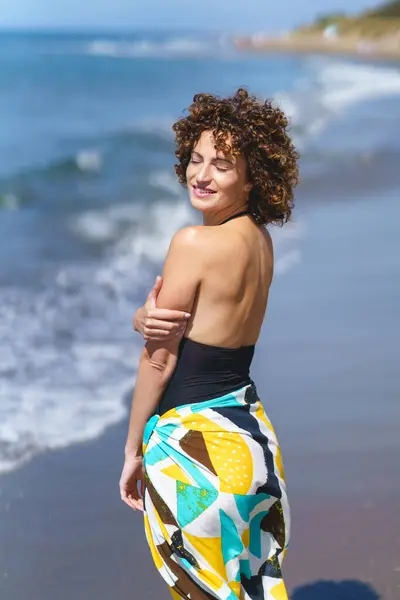 カジュアルなカラフルな服の若いセンセーショナルな女性の側面の景色は 日光の中で屋外風を楽しんでいる間 閉じた目で海岸に立っているカーリーヘア ロイヤリティフリーのストック写真