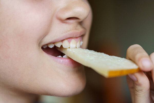 Closeup of happy anonymous teenage girl eating fresh cheese slice at home