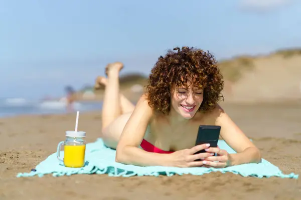 Młoda Kręcone Włosy Kobieta Bikini Leżące Piaszczystej Plaży Przeglądania Telefonu Obrazy Stockowe bez tantiem