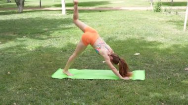 Çevresi yeşilliklerle çevrili huzurlu bir parkta, genç bir kadın yoga pozları veriyor, dayanıklılık ve esnekliği vurguluyor. Zindelik, sağlık ve refah konularına uygun