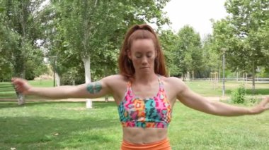 Renkli spor kıyafetleri giyen bir kadının spor, sağlık ve açık hava aktiviteleriyle ilgili konular için ideal bir manzara parkında esnediği görülüyor. Duruşu sağlık ve canlılık hissi veriyor.