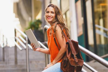 Şehirde dijital tablet kullanırken kameraya gülümseyen güzel Latin kadın.