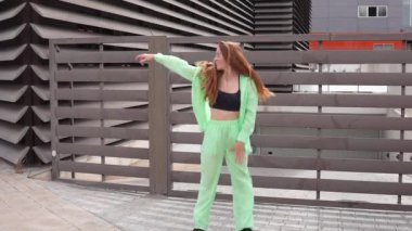 Canlı bir şehirde, çarpıcı yeşil takım elbiseli şık genç bir kadın hayat dolu bir enerjiyle dans ediyor, canlılık ve neşe saçıyor. Dinamik performansında özgüven ve bireyselliği somutlaştırıyor.