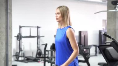 Çağdaş bir spor salonunda, kararlı genç bir kadın gücünü ve formununu korumak için ağırlık kaldırmaya odaklanır, kendini adamışlığını, motivasyonunu ve rutinini gösterir.