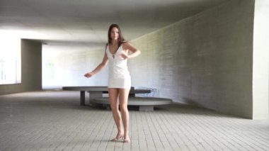 Zarif bir kadın, zarif bir şekilde beyaz bir elbise giyer, güzel bir modern, minimalist bir çevrede poz verir. Bu pozlar onun doğasında olan zarafeti ve inkar edilemez özgüvenini gösterir.